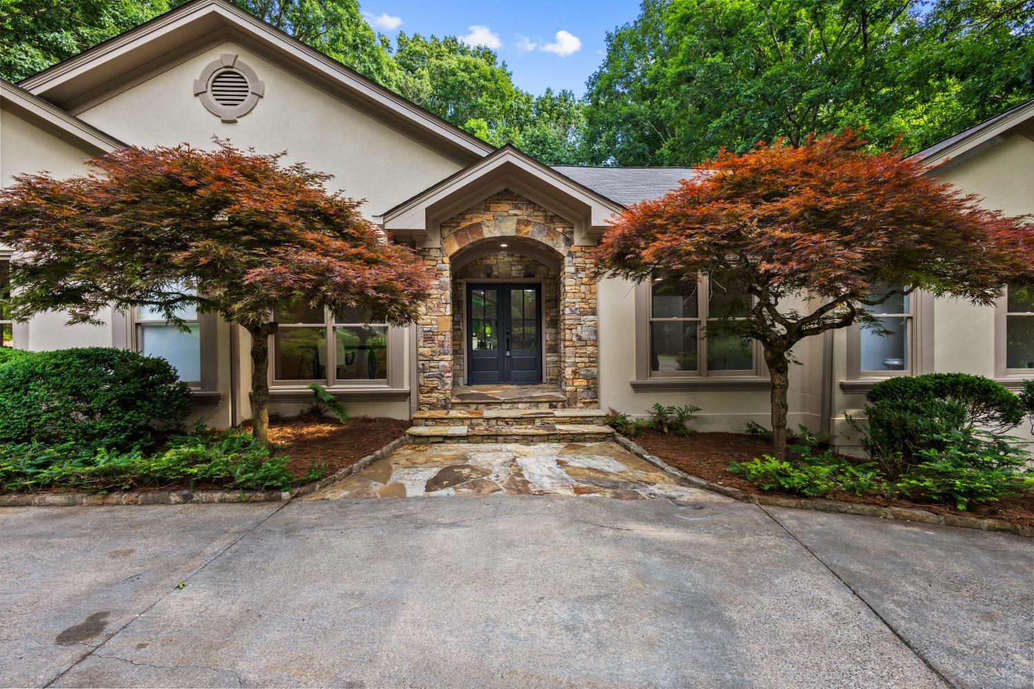 8920 Huntcliff Trace, Sandy Springs — the front elevation after JDT Capital's renovation: stone arched entry, two Japanese maples, flagstone walk